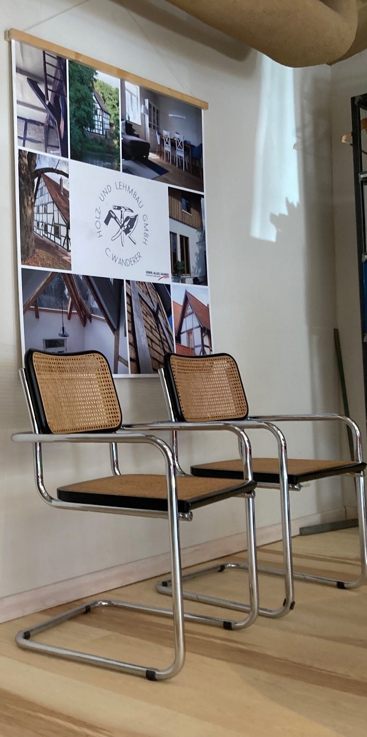 Thonet Stühle (Cesca) im Büro Zwei metallene Stühle (Modell Cesca von Thonet) mit geflochtener Sitzfläche vor einer Bilderwand.