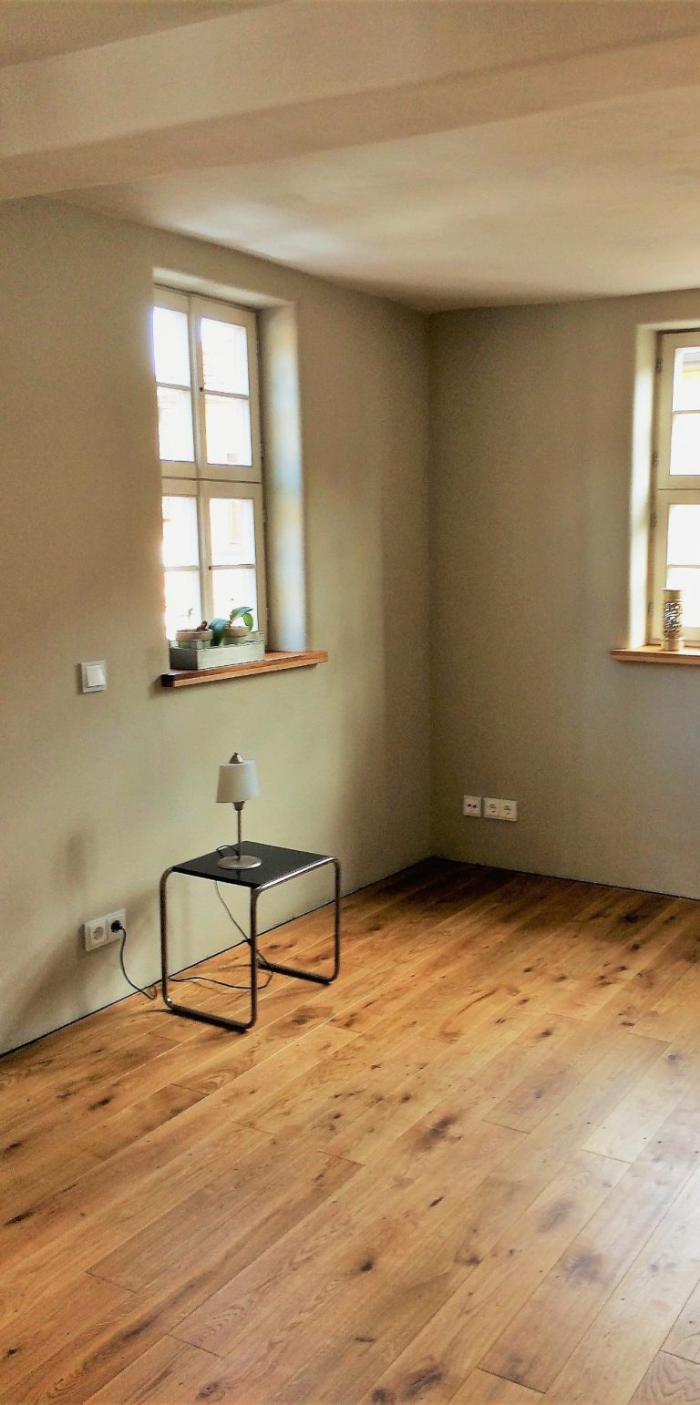 Innenraum gestaltet mit Holz und Lehm Innenraum mit Holzfußboden, zwei Fenstern, Lehmputz und einem Hocker.